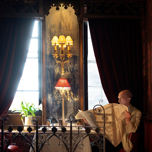 James Thomson reading a newspaper by a window in The Witchery Restaurant